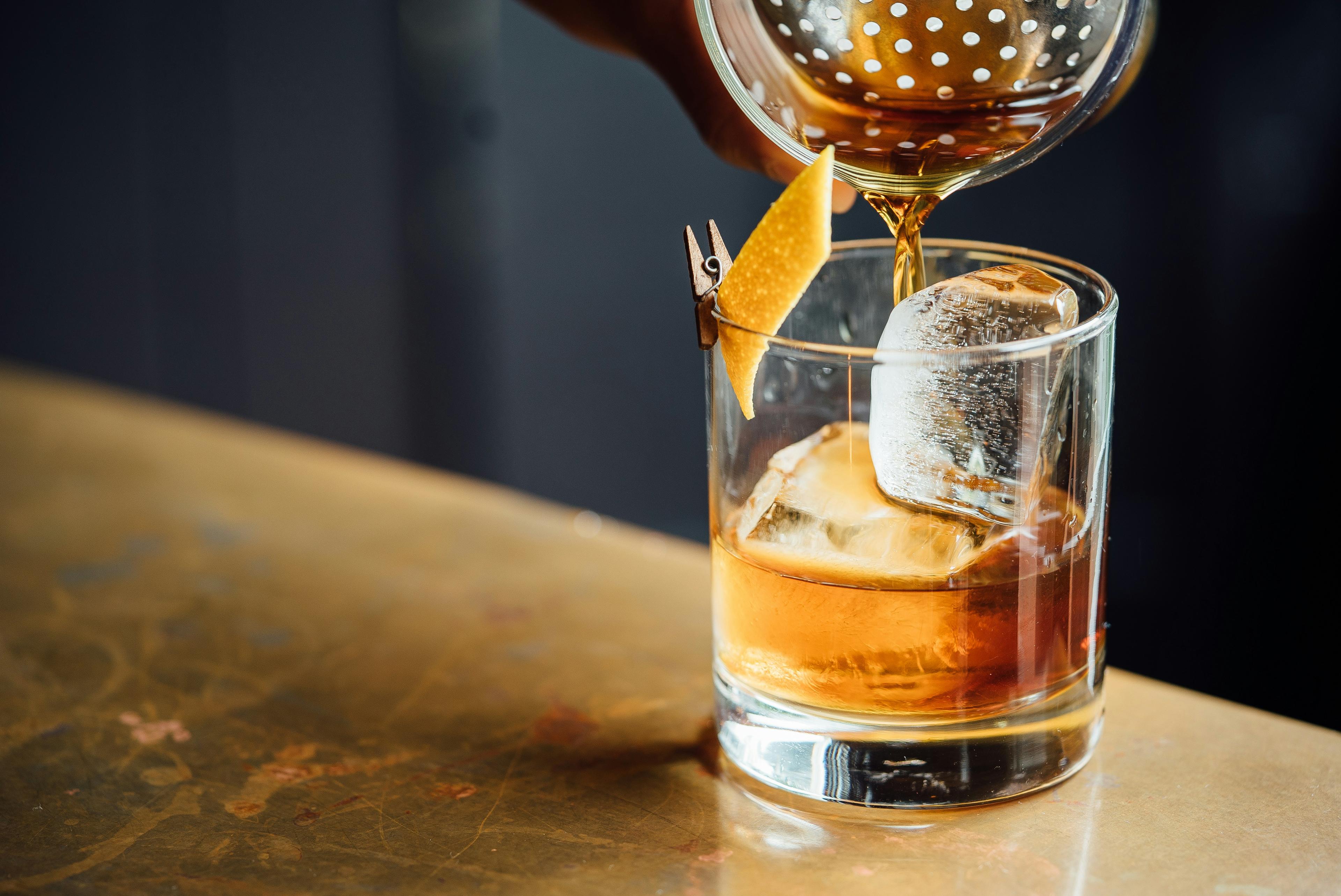 Cocktail a ser coado sobre um cubo de gelo
